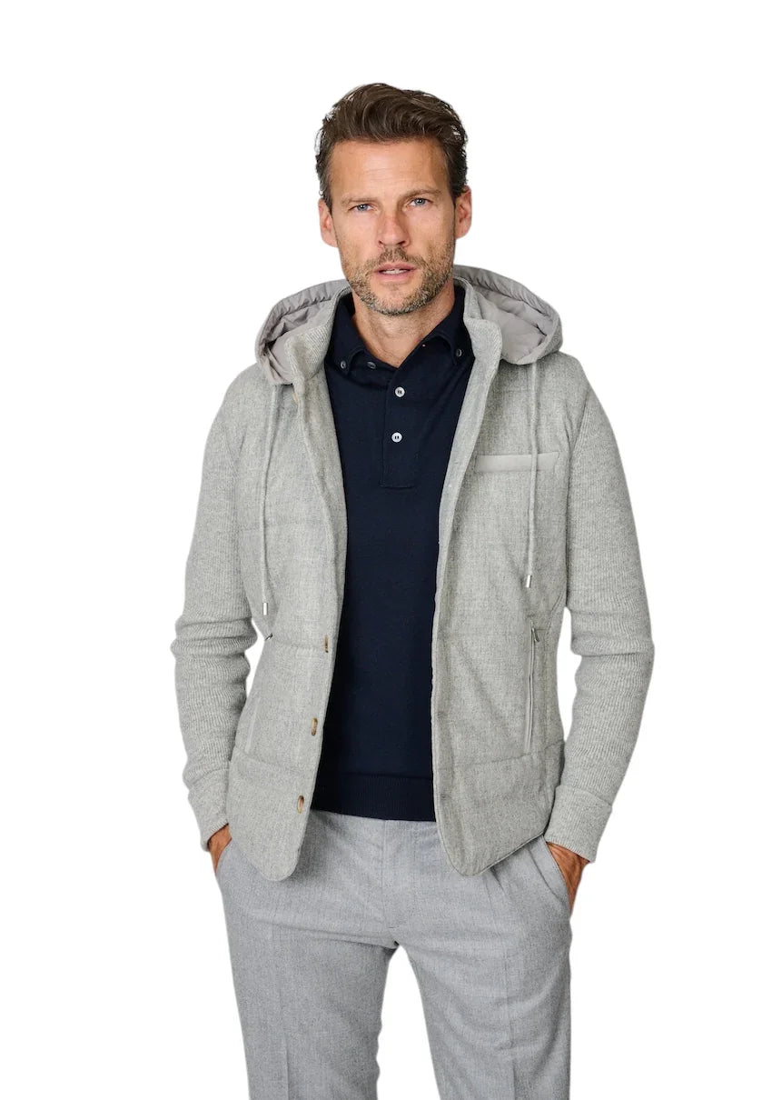 Man in een lichtgrijze hoodie over een donkerblauw poloshirt en grijze pantalon.