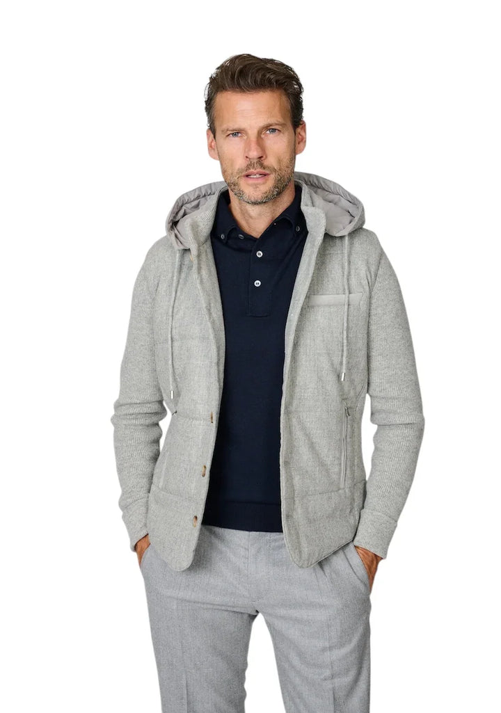 Man in een lichtgrijze hoodie over een donkerblauw poloshirt en grijze pantalon.