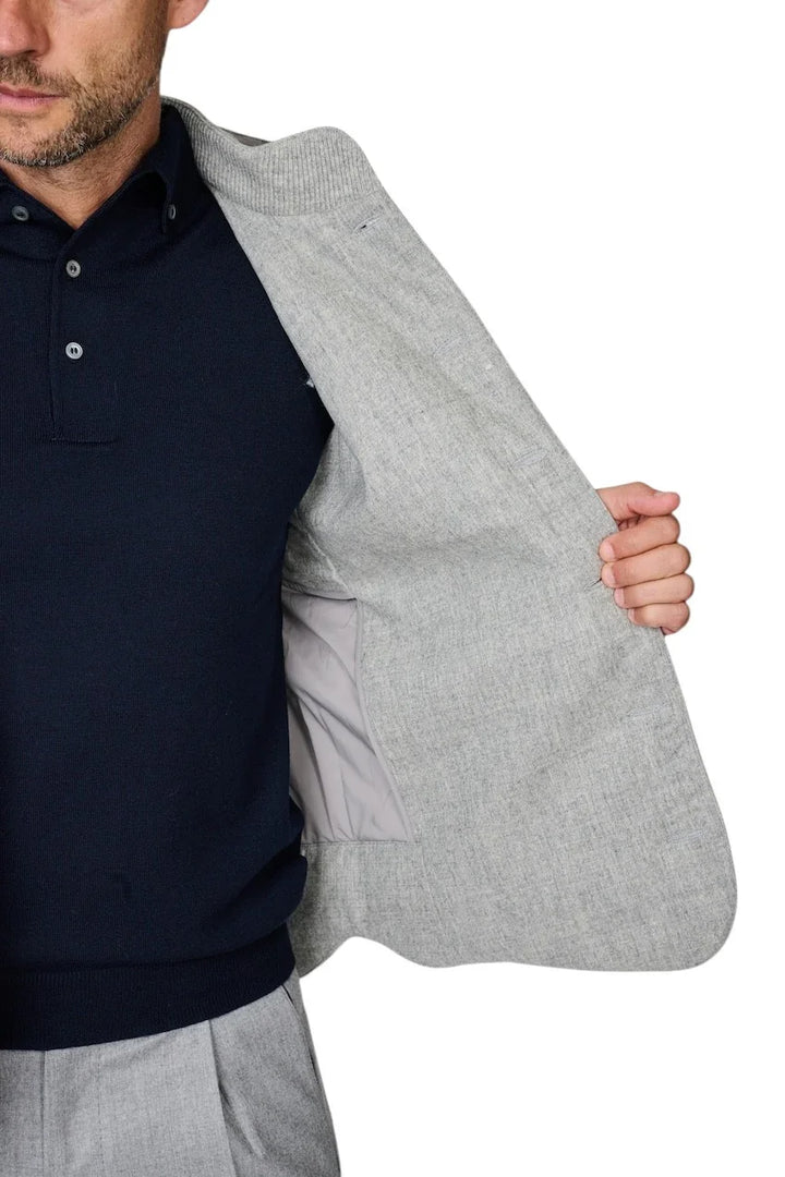Man met een donkerblauwe polo en een lichtgrijs colbert over de schouder.