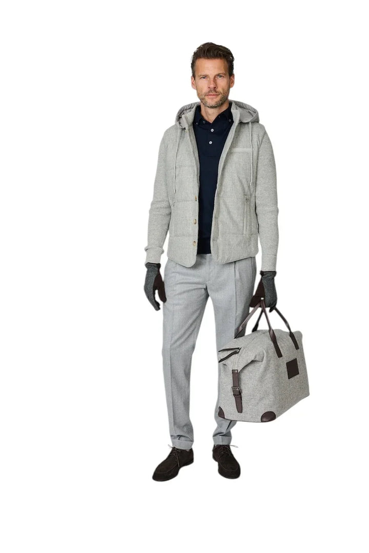 Man in een lichtgrijze jas, grijze pantalon en donkerblauwe polo met een grijze reistashas