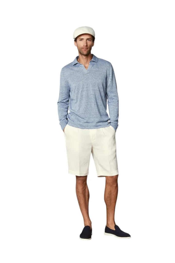 Man in een lichtblauwe polo met lange mouwen, witte korte broek en donkerblauwe instappers.