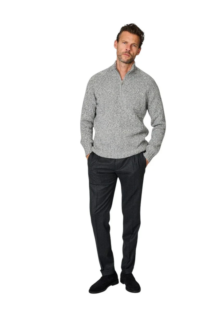 Man in een grijze gebreide trui met ritssluiting en een donkergrijze pantalon.