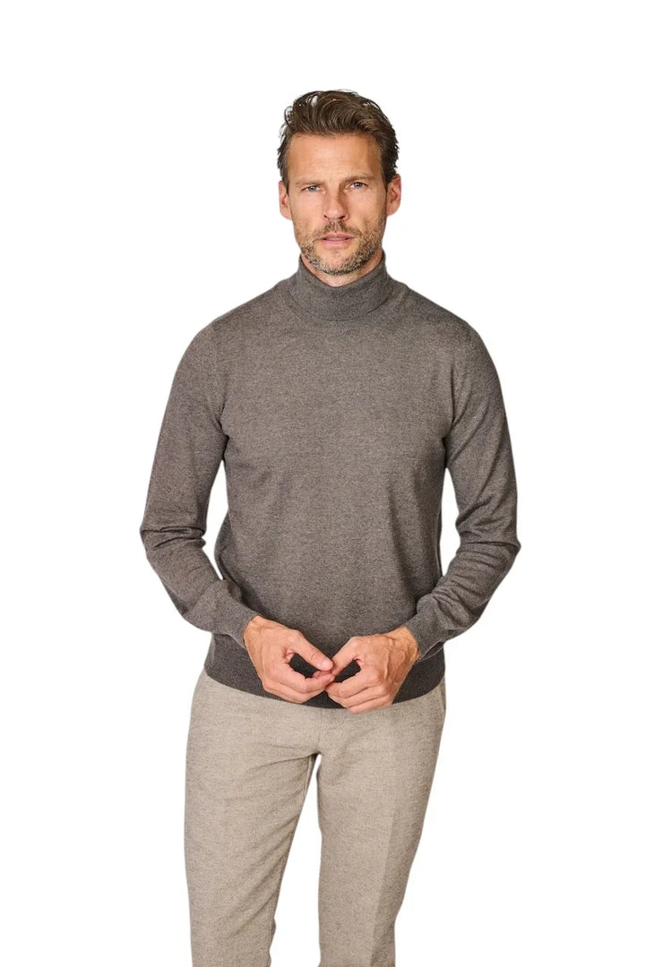 Man in een bruine coltrui en beige pantalon tegen een witte achtergrond.
