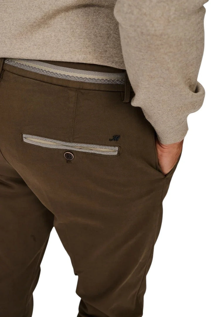 Detail van een bruine herenpantalon met contrastrijk wit biesje bij de taille en zak.