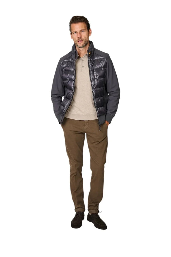 Man in een grijs gewatteerd hybride jack, beige polo en bruine chino broek.