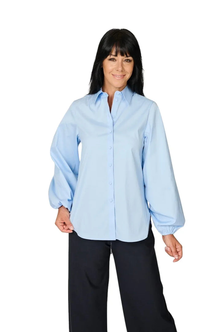 Vrouw in een lichtblauwe blouse met pofmouwen en een zwarte pantalon.