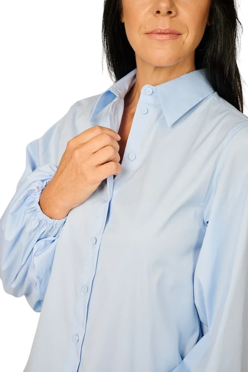 Vrouw in een lichtblauwe blouse met lange mouwen en knoopsluiting