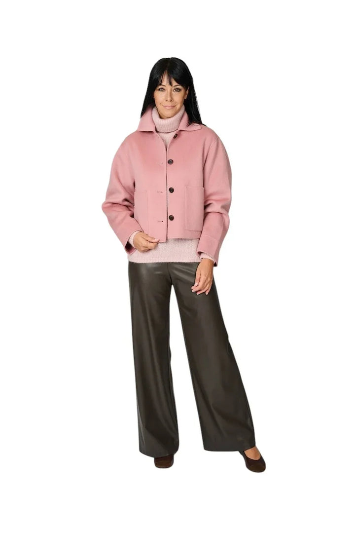 Vrouw in roze jasje, roze coltrui en een bruine leren wijde broek.