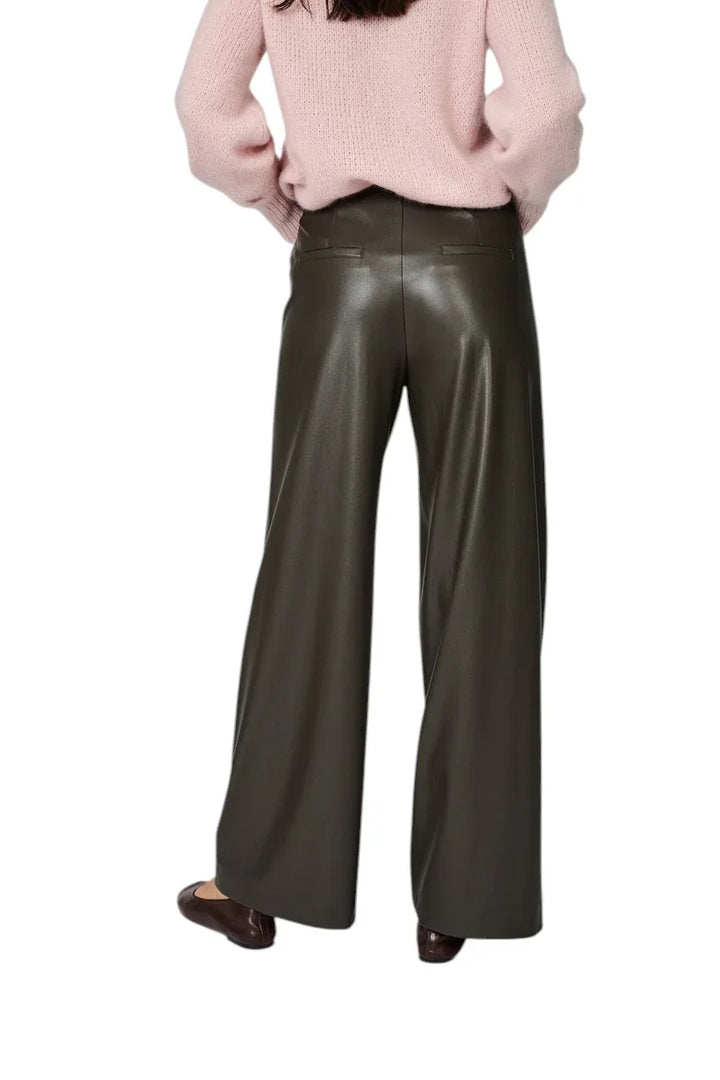 Dame in een roze gebreide trui en een donkergroene leren wijde pantalon.