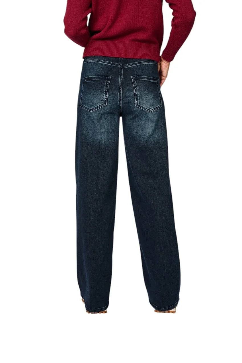 Achterzijde van een donkerblauwe damesjeans met wijdere pijpen en een rode trui.